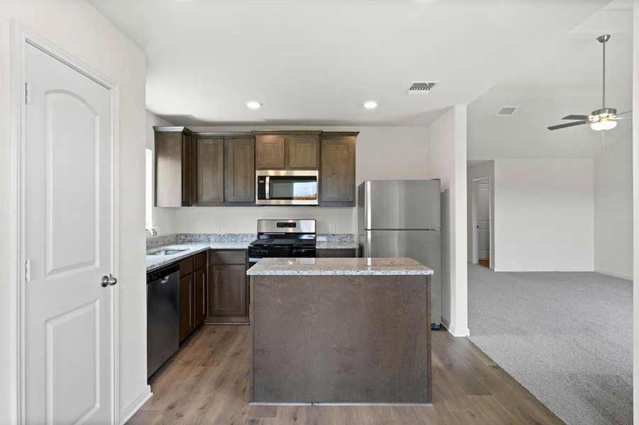 Kitchen with stainless steel appliances, a center island, dark brown cabinets, recessed lighting, and light stone countertops Kitchen with stainless steel appliances, a center island, dark brown cabinets, recessed lighting, and light stone countertops