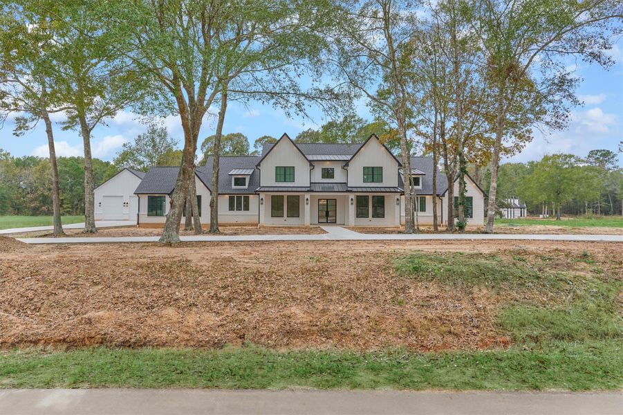 Beautiful modern farmhouse façade framed by mature trees, offering serene curb appeal and a welcoming approach from the roadside.