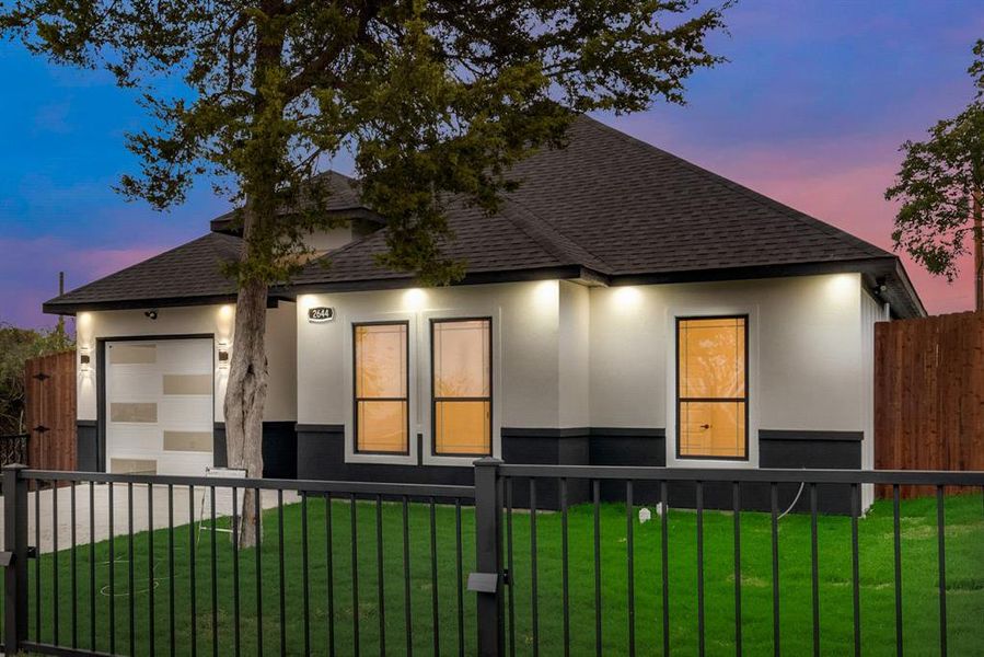 Property exterior at dusk with a one car garage, large front lawn and gate.