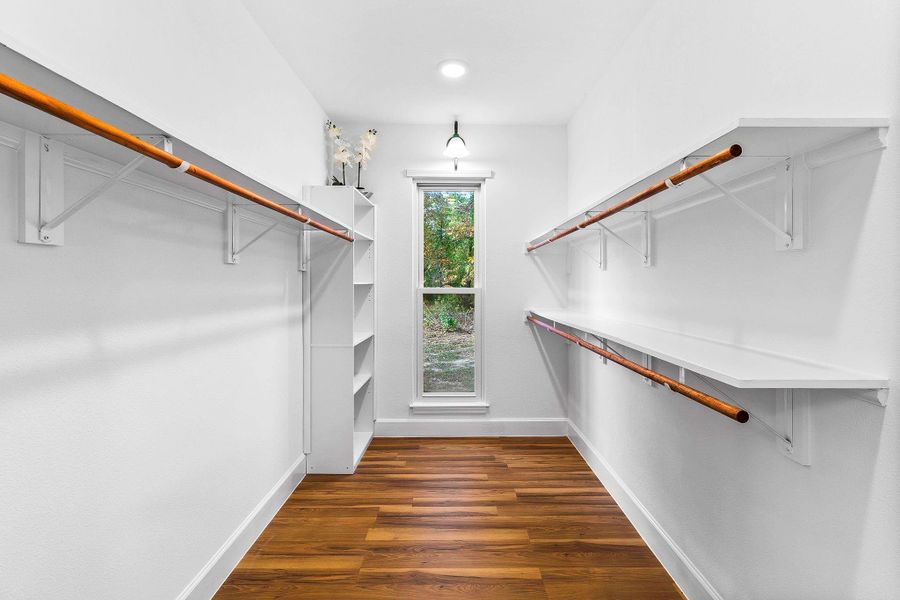 This spacious walk-in closet features elegant wooden flooring, ample shelving, and hanging space, with a large window for natural light. Perfect for organizing your wardrobe.