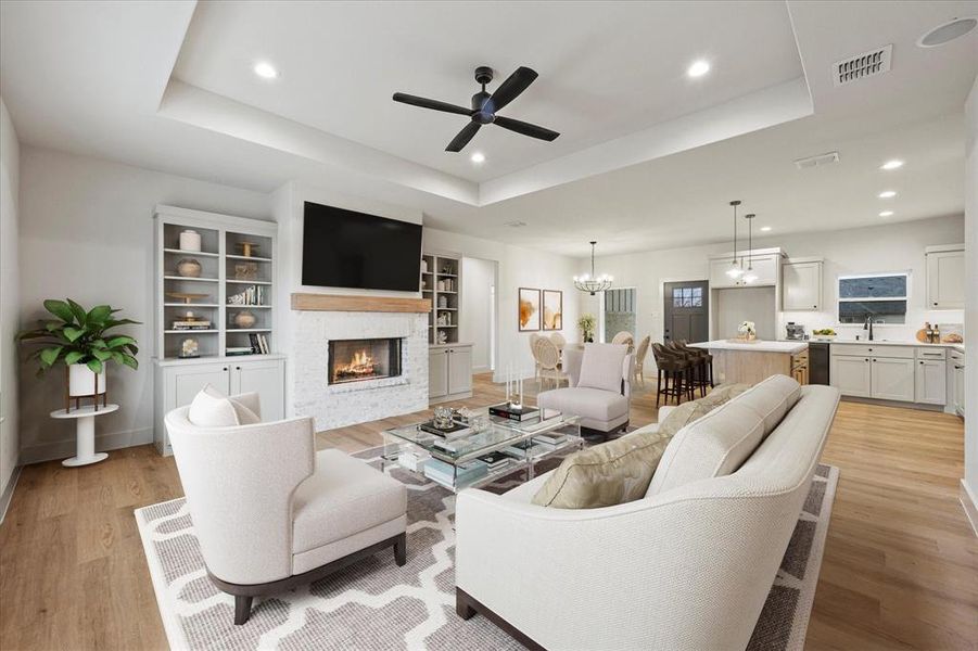 Living room featuring a tray ceiling, a stone fireplace, ceiling fan with notable chandelier, and light hardwood / wood-style flooring