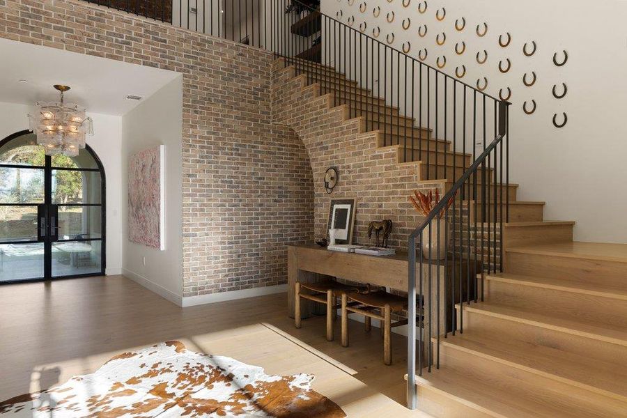Staircase with brick wall, wood finished floors, and hanging lights