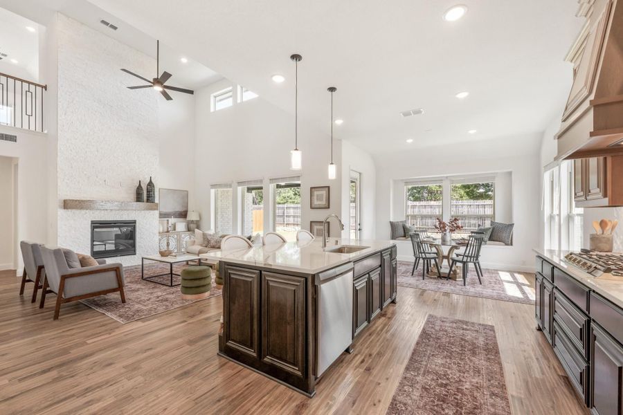 Open-concept living area with kitchen island, dark cabinets, stone fireplace, and hardwood floors