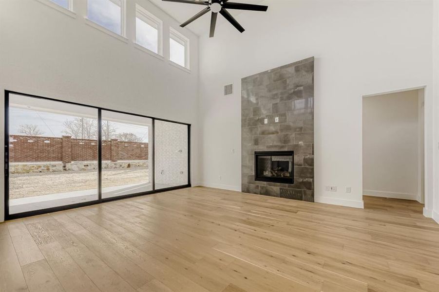 Unfurnished living room featuring a tile fireplace, ceiling fan, a high ceiling, and light wood-style flooring