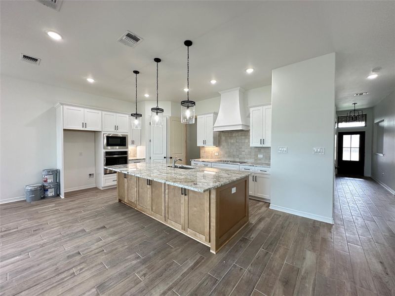 Kitchen featuring white cabinetry, light stone countertops, a large island with sink, decorative backsplash, and hanging light fixtures