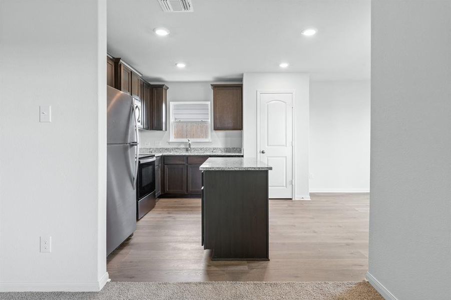 Kitchen with a kitchen island, stainless steel appliances, dark brown cabinets, recessed lighting, and light wood finished floors