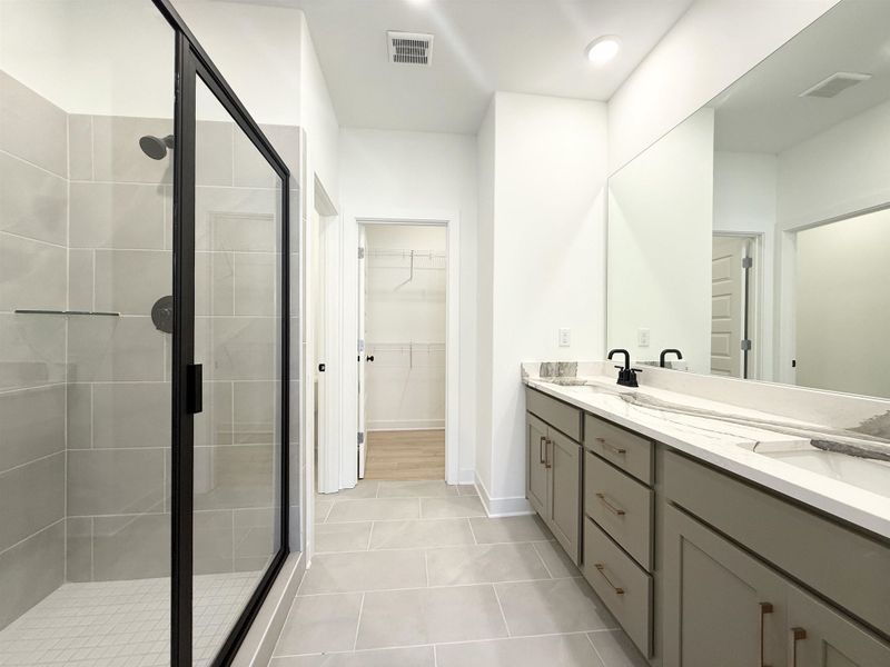 Full bathroom with double vanity, a shower stall, light tile patterned flooring, and a spacious closet