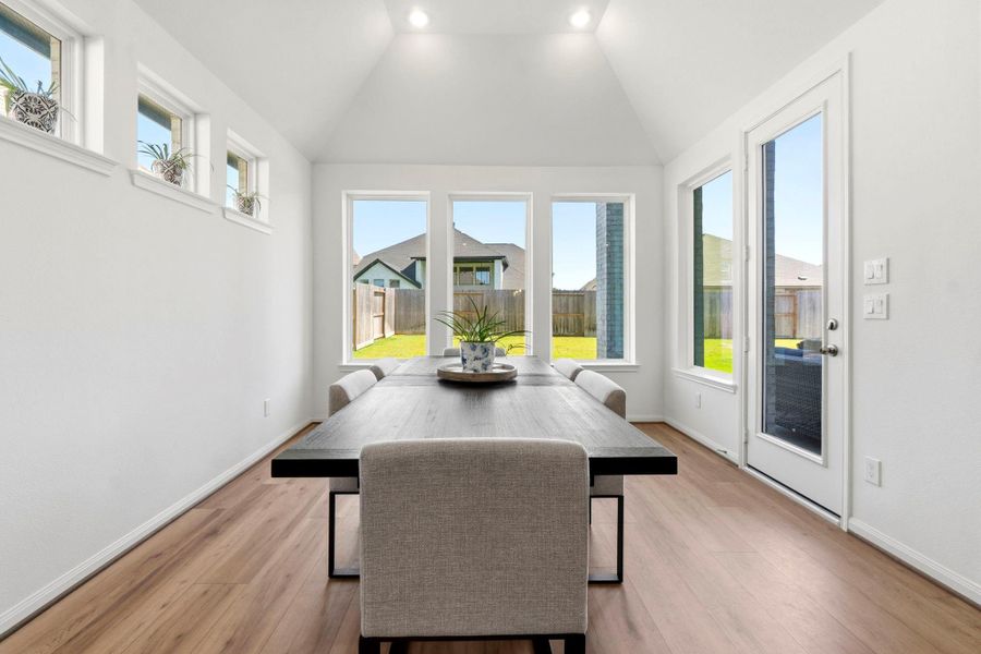 Bright, modern dining area with high ceilings and large windows offering plenty of natural light. View of the backyard through glass doors.