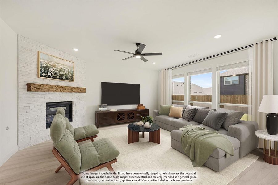 Living room with stone fireplace, gray sectional sofa, ceiling fan, and large windows with natural light