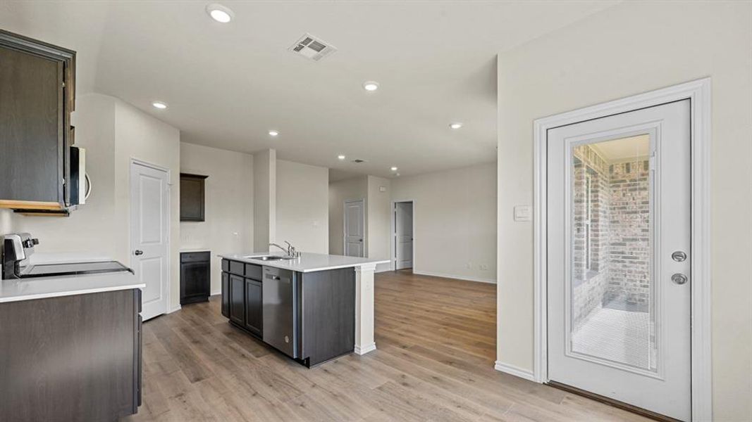 Kitchen featuring a kitchen island with sink, stainless steel appliances, light wood-style flooring, recessed lighting, and dark wood finish cabinetry