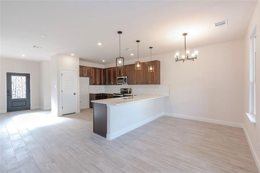 Kitchen with light hardwood / wood-style flooring, kitchen peninsula, stainless steel appliances, sink, and decorative light fixtures