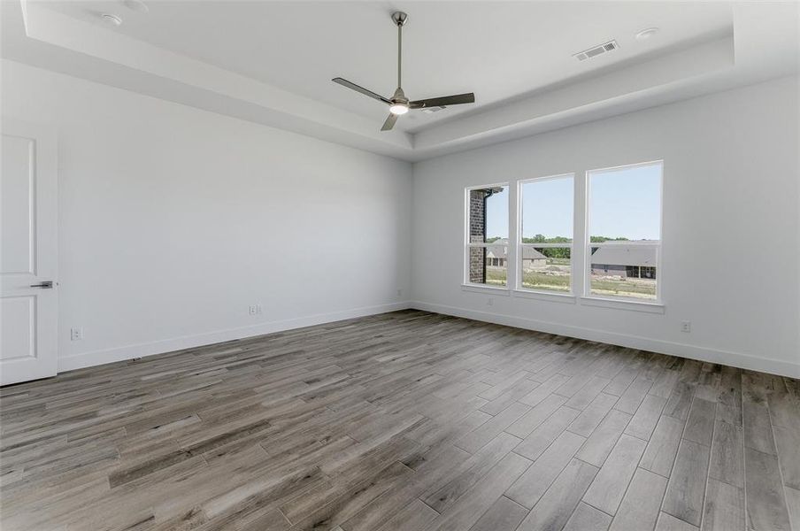 Spacious room featuring wood-finish flooring, a tray ceiling, and a modern ceiling fan