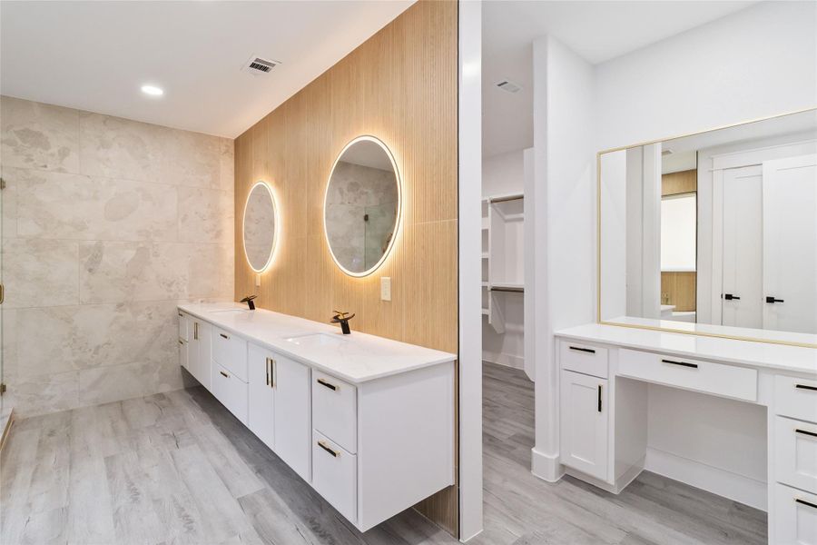 Full bath with tile walls, double vanity, a spacious closet, light wood finished floors, and a shower with door