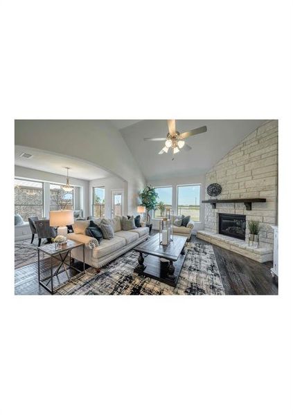 Living room featuring vaulted ceiling, ceiling fan, hardwood / wood-style floors, and a stone fireplace