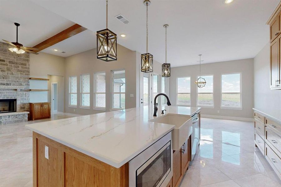 Kitchen featuring appliances with stainless steel finishes, a fireplace, a kitchen island with sink, and beamed ceiling