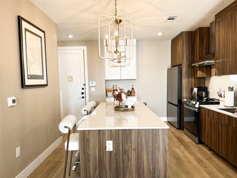 Kitchen featuring a kitchen breakfast bar, a kitchen island, stainless steel appliances, light wood-type flooring, and light stone countertops