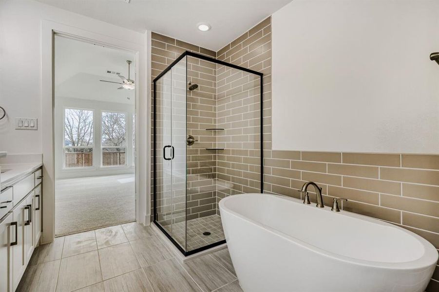 Bathroom featuring a shower stall, a soaking tub, tile walls, vanity, and ceiling fan