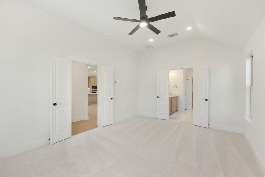 Empty bedroom with carpet, ceiling fan, and open doors leading to bathroom and hallway
