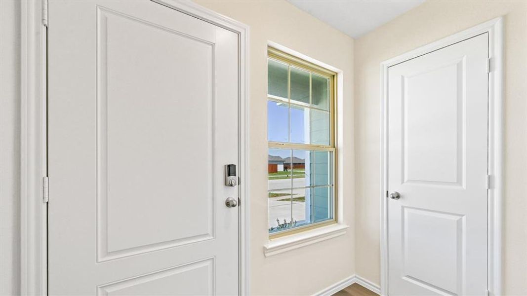 Entryway featuring a white paneled door with smart lock hardware, a double-hung window with a golden-hued frame, and light-toned walls Entryway featuring a white paneled door with smart lock hardware, a double-hung window with a golden-hued frame, and light-toned walls