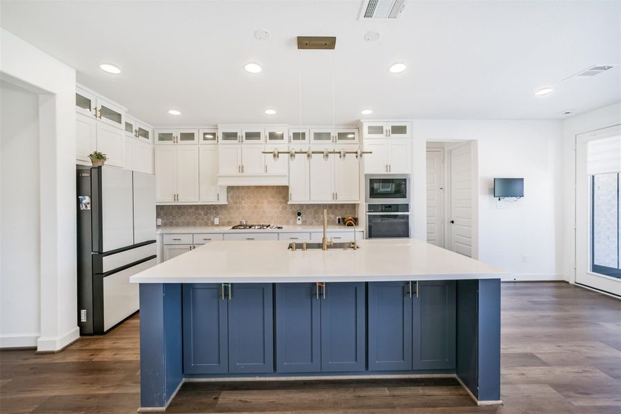 A central island featuring a sleek breakfast bar, a quartz countertop, and an undermount sink. Beautifully extended cabinets with elegant glass panels add a touch of sophistication, complemented by soft, recessed lighting for a warm and inviting ambiance. A central island featuring a sleek breakfast bar, a quartz countertop, and an undermount sink. Beautifully extended cabinets with elegant glass panels add a touch of sophistication, complemented by soft, recessed lighting for a warm and inviting ambiance.