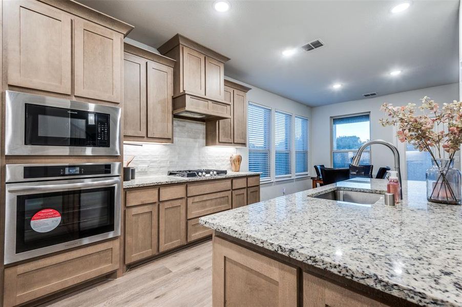 Kitchen with stainless steel appliances, decorative backsplash, light wood-style floors, light stone counters, and recessed lighting Kitchen with stainless steel appliances, decorative backsplash, light wood-style floors, light stone counters, and recessed lighting
