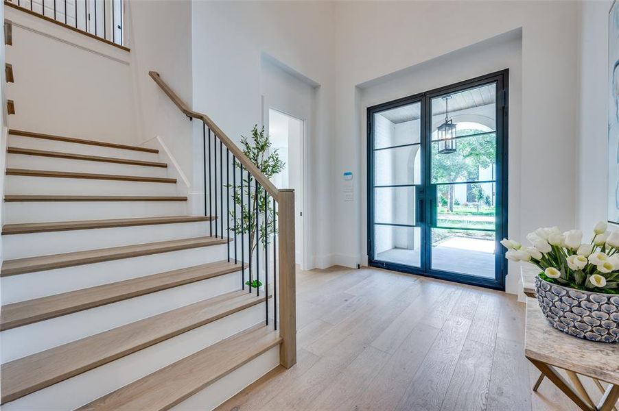 Entryway featuring light wood-type flooring, stairway, a chandelier, and a towering ceiling
