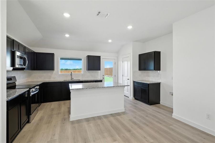 Kitchen featuring vaulted ceiling, stainless steel appliances, tasteful backsplash, a center island, and light stone counters Kitchen featuring vaulted ceiling, stainless steel appliances, tasteful backsplash, a center island, and light stone counters