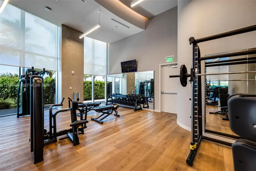 Fitness center featuring floor-to-ceiling windows, wood-finish flooring, high ceilings with recessed lighting, and full-wall mirrors