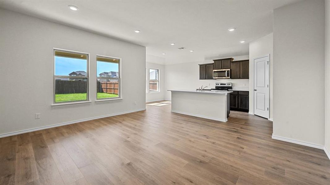 Kitchen featuring open floor plan, an island with sink, light countertops, dark wood finish cabinets, and healthy amount of natural light