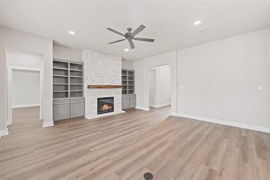 Unfurnished living room featuring light wood finished floors, ceiling fan, a stone fireplace, recessed lighting, and built in shelves