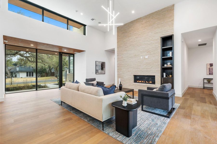 Living room with light wood-style floors, a fireplace, a high ceiling, and a chandelier