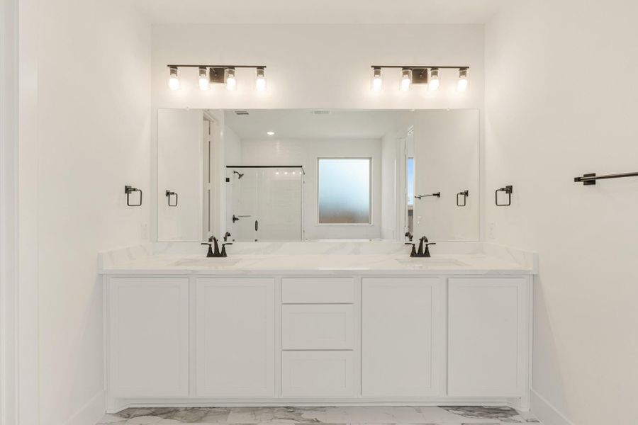 Bathroom with double vanity, white cabinets, quartz countertop, large mirror, and black fixtures