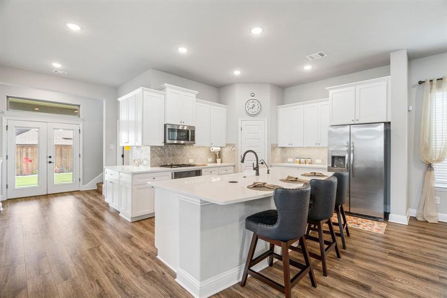 Modern kitchen featuring white cabinetry, stainless steel appliances, a center island with countertop seating, and wood-finish flooring Modern kitchen featuring white cabinetry, stainless steel appliances, a center island with countertop seating, and wood-finish flooring