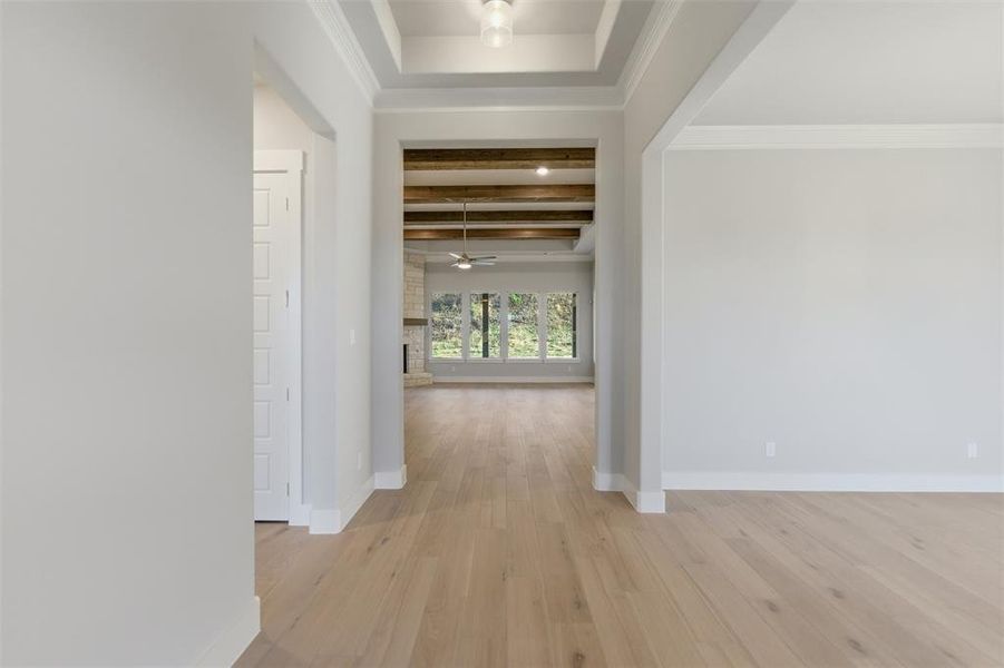 Hall with light wood finished floors, beamed ceiling, and crown molding