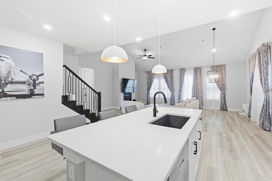 Kitchen featuring ceiling fan, an island with sink, decorative light fixtures, light wood-style floors, and high vaulted ceiling