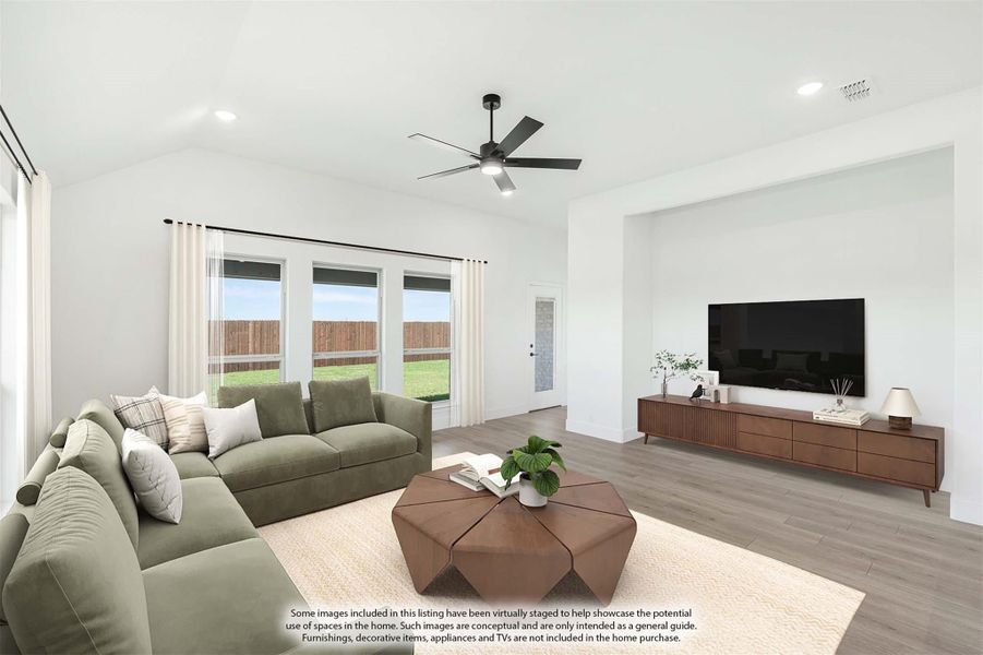Living room with vaulted ceiling, ceiling fan, hardwood floors, green sectional sofa, and large windows with backyard view