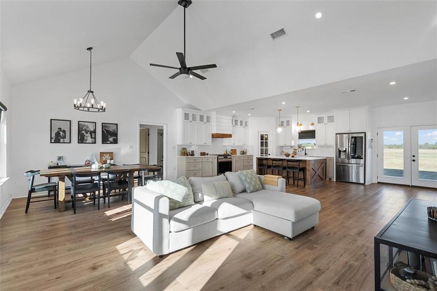Living area featuring high vaulted ceiling, dark wood-type flooring, a chandelier, a ceiling fan, and french doors