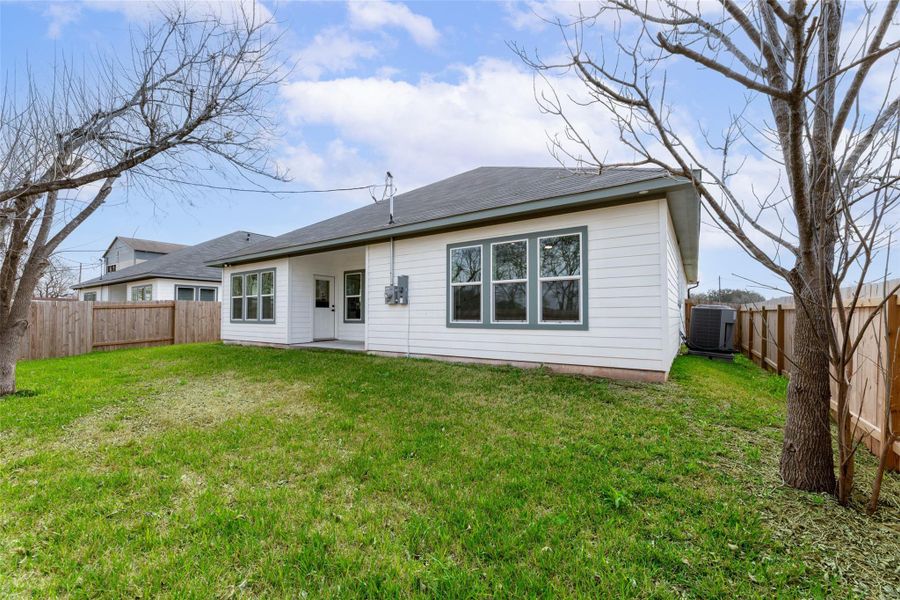 Backyard with a well-maintained lawn, enclosed by a wooden fence. The house features large windows and a simple exterior, providing a spacious and private outdoor area.