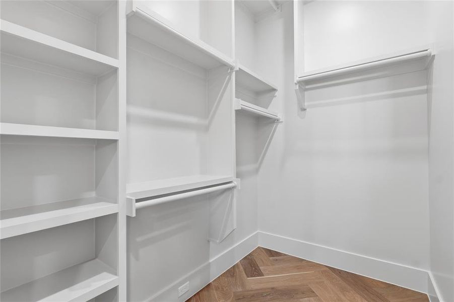Primary walk-in closet with custom built-ins, herringbone hardwood floors, and direct access to laundry room Primary walk-in closet with custom built-ins, herringbone hardwood floors, and direct access to laundry room