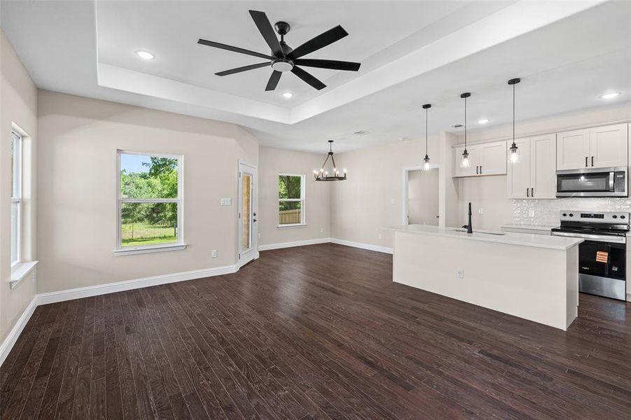Expansive open-concept living area featuring wood-finish flooring, a tray ceiling with a contemporary ceiling fan, and recessed lighting