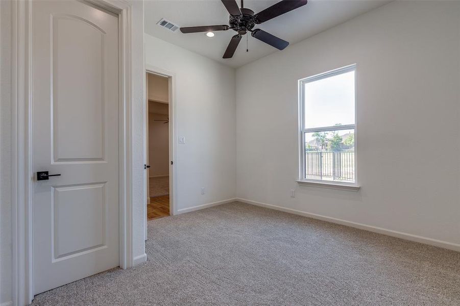 Unfurnished bedroom featuring multiple windows, ceiling fan, light carpet, and a walk in closet