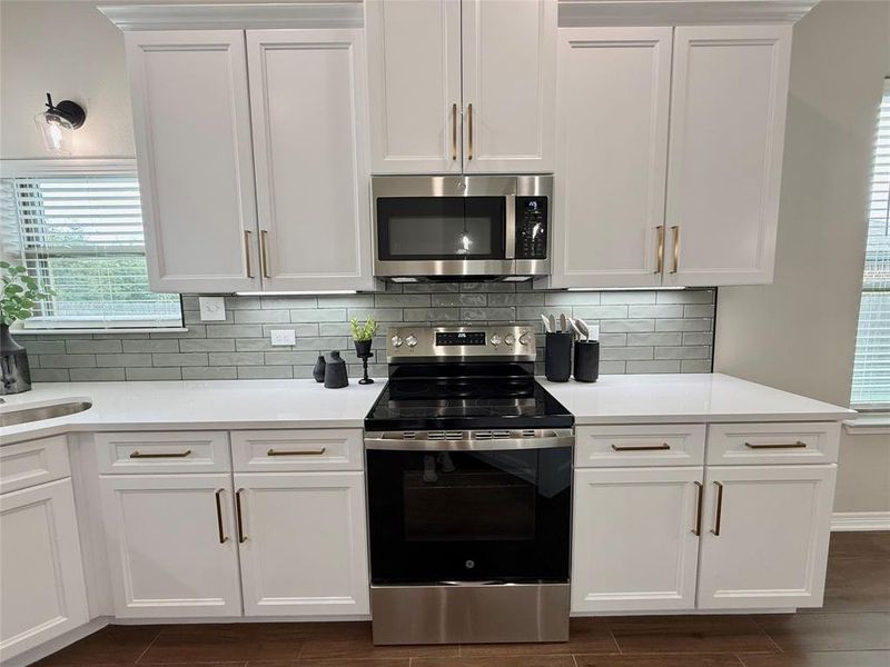 Kitchen featuring stainless steel appliances, white cabinetry, decorative backsplash, and light stone countertops Kitchen featuring stainless steel appliances, white cabinetry, decorative backsplash, and light stone countertops