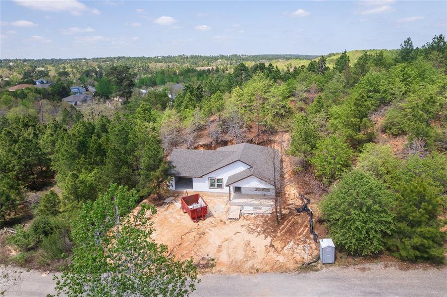 The property features a white exterior, a grey roof, and is surrounded by numerous trees and natural landscaping