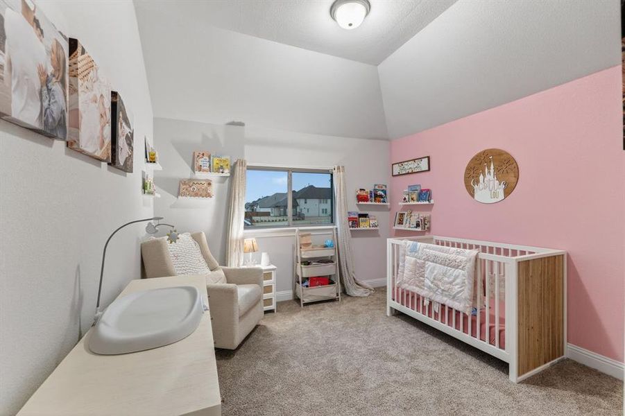 Bedroom featuring a nursery area, light colored carpet, and vaulted ceiling Bedroom featuring a nursery area, light colored carpet, and vaulted ceiling