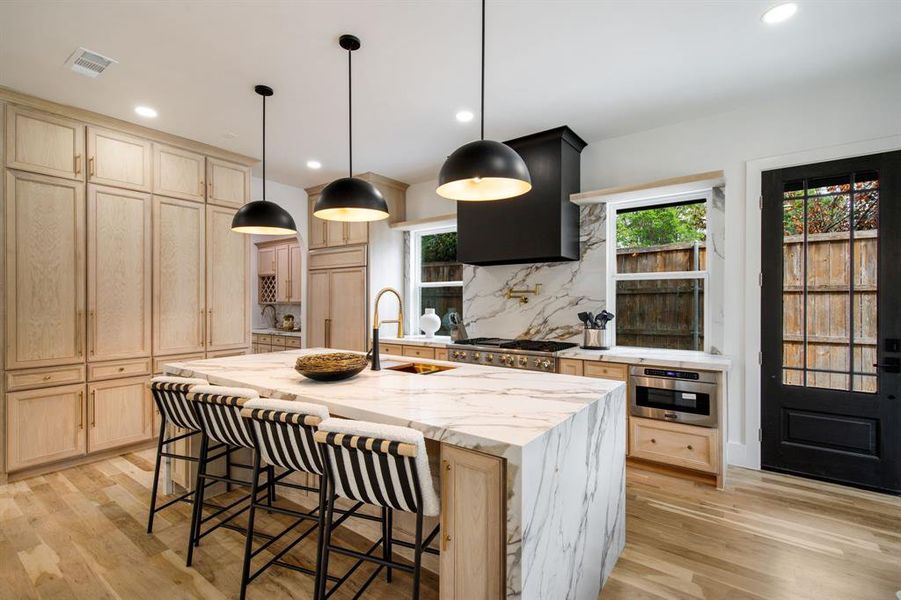 Gourmet kitchen featuring a waterfall island with stone countertop, natural wood cabinetry, a built-in range, and a built-in microwave Gourmet kitchen featuring a waterfall island with stone countertop, natural wood cabinetry, a built-in range, and a built-in microwave