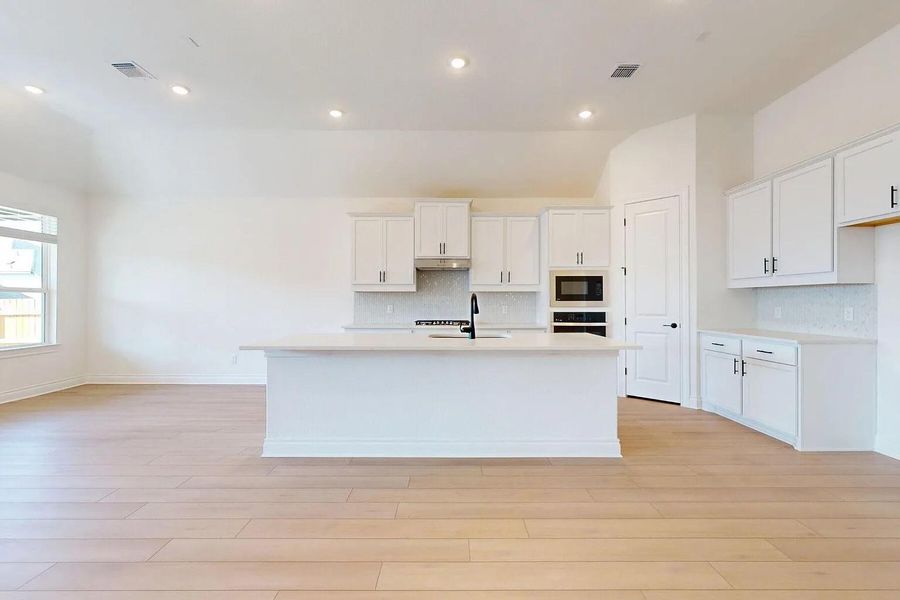 Kitchen featuring an island with a sink, white cabinetry, a built-in microwave, and hardwood floors