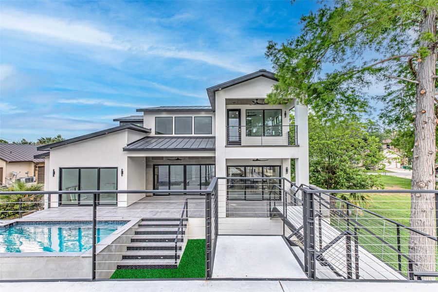 Back of property featuring stucco siding, an outdoor pool, a balcony, a standing seam roof, and metal roof