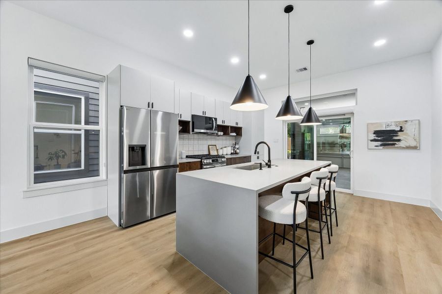 Rich walnut cabinetry, concrete inspired quartz surfaces, oversized waterfall island, matte black fixtures, and sculptural lighting create a kitchen that feels more boutique hotel than builder grade.