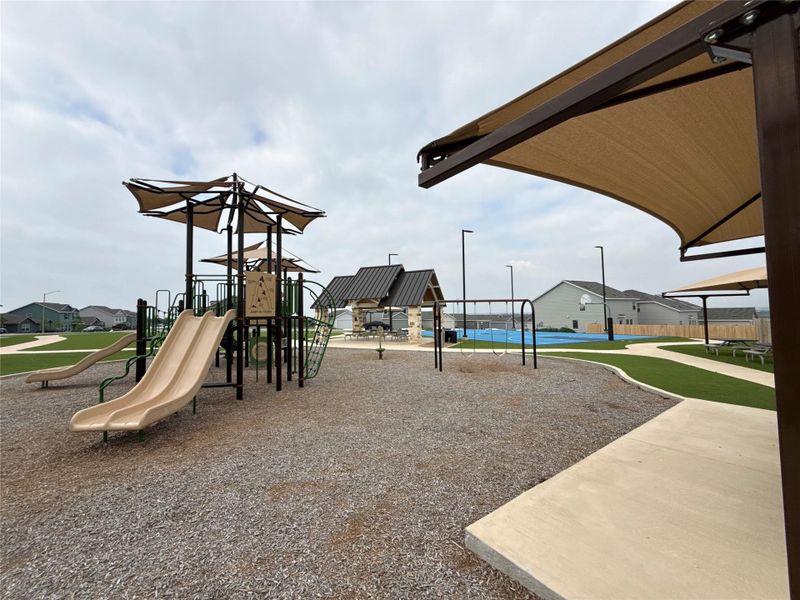 Community playground featuring multiple slides, shaded play structures, swings, and a basketball court