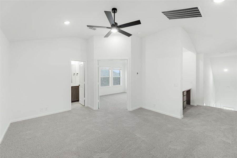 Spacious empty bedroom with vaulted ceiling, black ceiling fan, gray carpet, and open bathroom door Spacious empty bedroom with vaulted ceiling, black ceiling fan, gray carpet, and open bathroom door